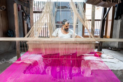 Preview: Indian man sitting at handloom weaving with purple thread
