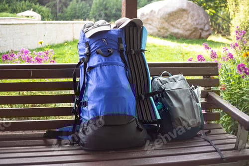 Preview: On a sunny summer day, two hiking backpacks on a park bench surrounded by bright flowers
