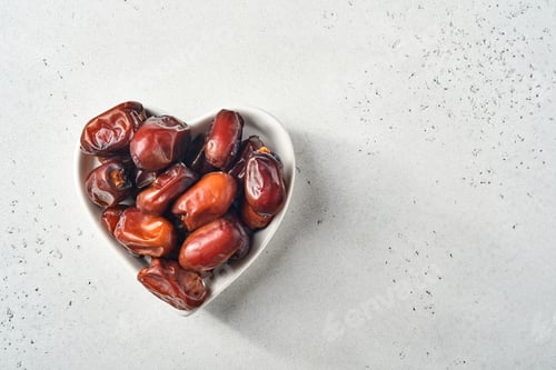 Preview: Dried sliced date fruit in a heart-shaped ceramic plate on white background with copy space. Snack v