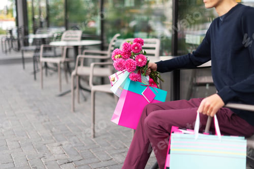 Preview: Boyfriend waiting for his girlfriend near cafe and holding flowers bouquet and bunch of pink gift