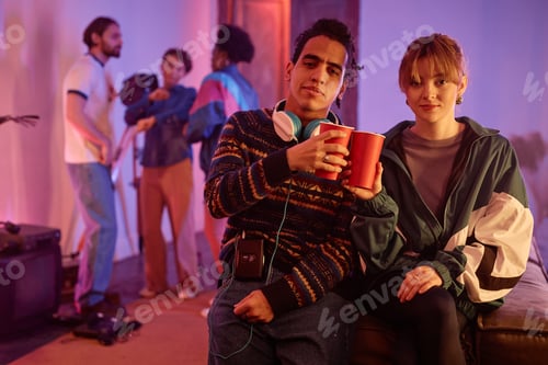 Preview: Retro styled young couple at house party holding red cups and