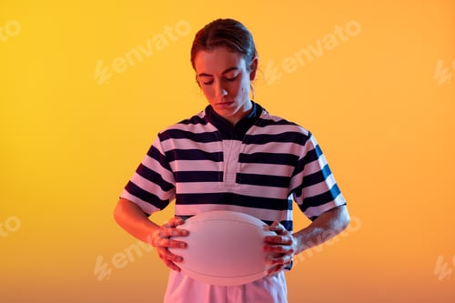 Preview: Caucasian female rugby player with rugby ball over neon yellow lighting