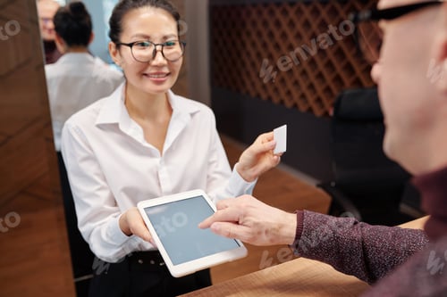 Preview: Hand of mature businessman over tablet display and young receptionist with card