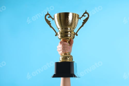 Preview: Woman holding gold trophy cup on light blue background, closeup