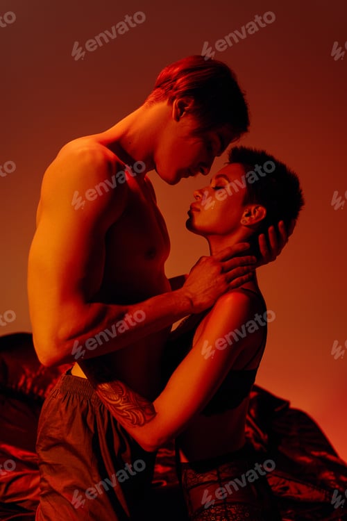 Preview: side view of young shirtless man hugging passionate woman in bra on red background