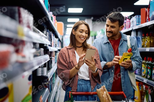 Preview: Happy couple using smart phone while buying in a supermarket.