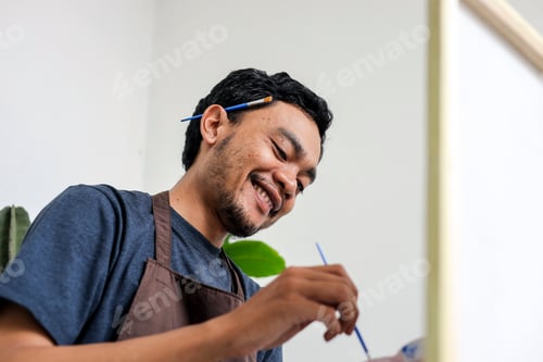 Preview: Close Up Of Cheerful Young Artist Man While Painting On Canvas With Paintbrush