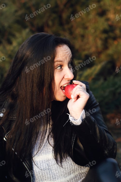Preview: Pretty young woman holding a red apple in her hand and biting it
