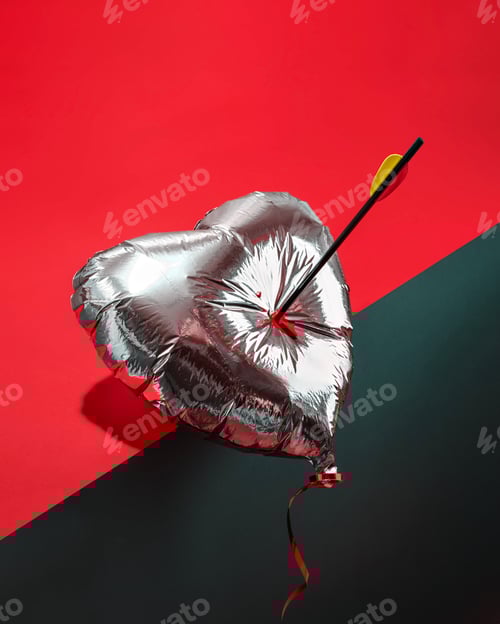 Preview: Metallic heart balloon skewered by an arrow on a vivid red and black backdrop