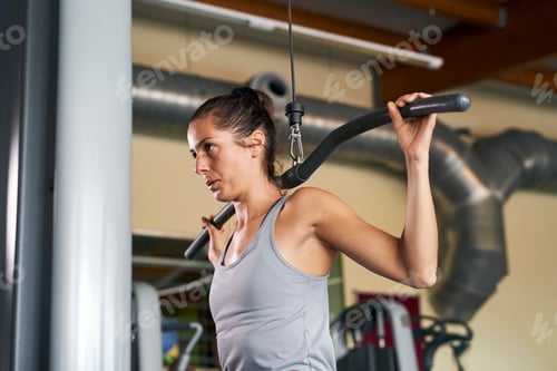 Preview: Beautiful young woman in sports shorts and a gray tank top engaged in fitness in the gym