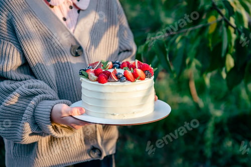 Preview: Unrecognizable girl holding white tasty cake decorated with fresh berries. Natural light and shadow