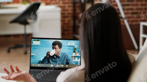 Preview: Young adult woman talking to coworker on laptop virtual videocall meeting while working remotely