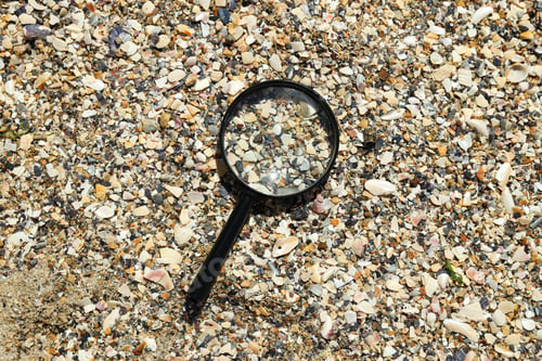 Preview: A magnifying glass lies on the sand by the river