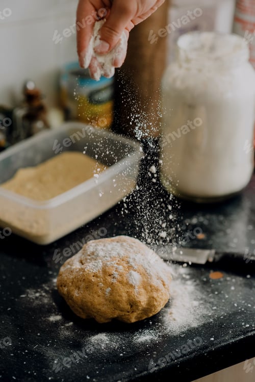 Preview: Vertical shot of a hand sprinkling flour on a dough ball on the table