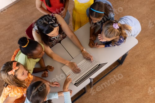 Preview: High angle view of diverse female teacher teaching schoolgirls over laptop at desk in classroom