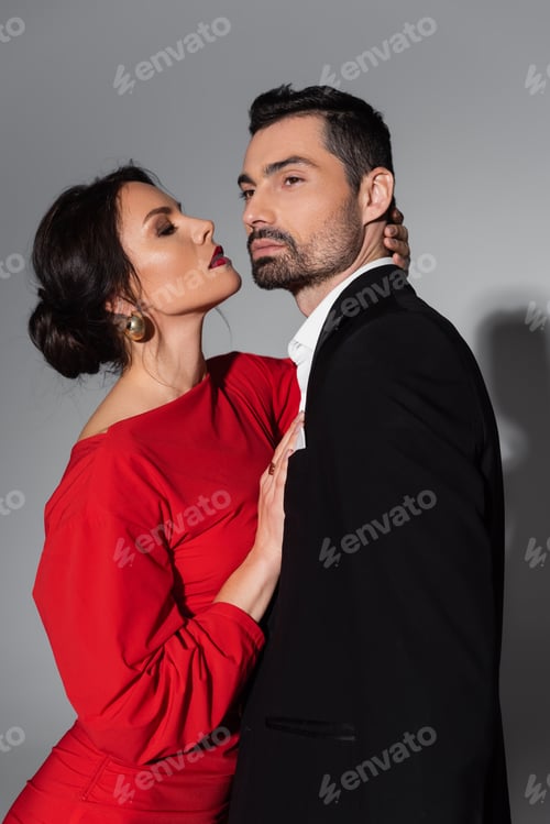 Preview: Sexy woman with burgundy lips hugging bearded boyfriend on grey background