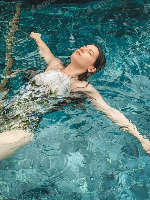 Preview: Young woman floating at the pool during tropical rain. Relaxing and quality time in vacation.