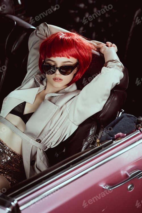Preview: high angle view of stylish girl in trench coat and sunglasses sitting in retro car