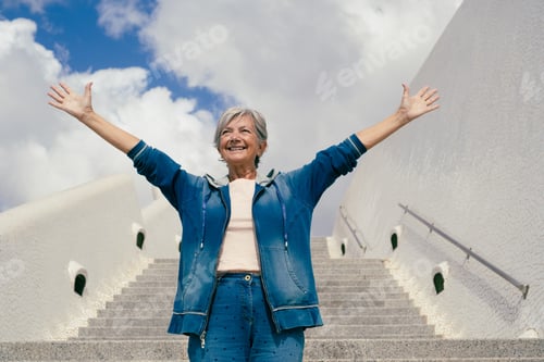 Preview: Smiling senior woman with outstretched arms outdoors on staircases enjoying freedom and travel