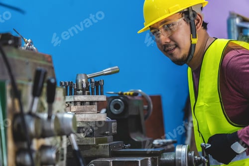 Preview: Asian machinist in safety suit operating the professional lathes in metalworking factory,