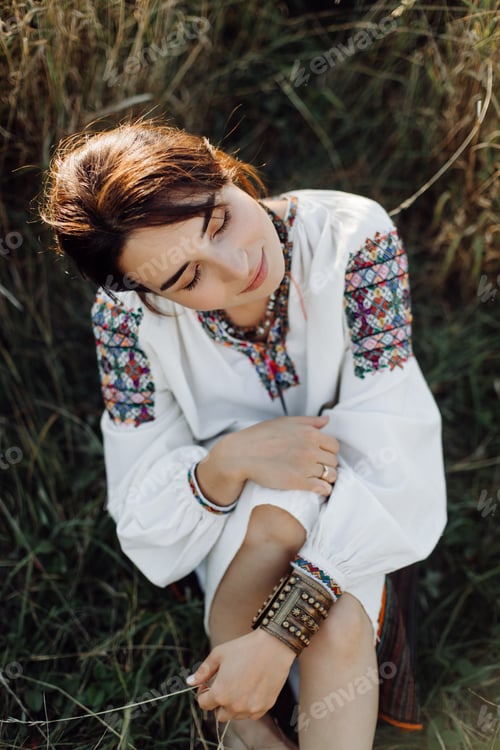 Preview: Young woman in traditional national embroidered shirt and skirt on nature at sunset.