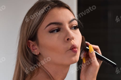 Preview: Young woman, teenage girl is applying make up with a brush in a bathroom, getting ready to go out