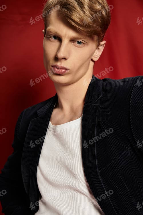 Preview: Young alluring man exudes modern masculinity in stylish pose against bold red backdrop