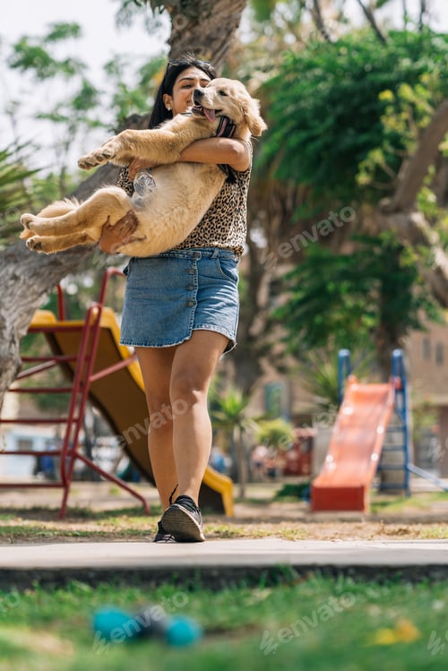 Preview: Woman carrying in arms a puppy dog in a park