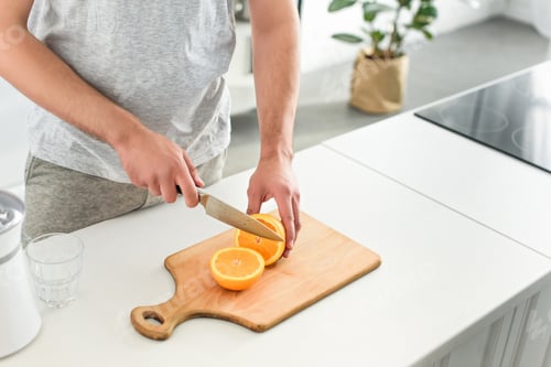 Preview: cropped image of man cutting oranges by knife on tabletop