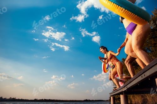 Preview: Group of friends having fun enjoying a summer day jumping at the lake while holding hands.