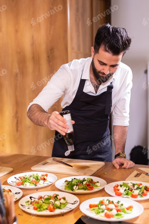 Preview: Chef pouring dressing over caprese salad in restaurant kitchen