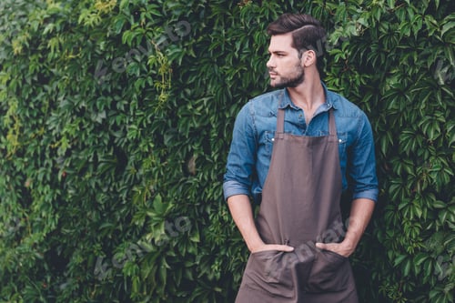 Preview: portrait of thoughtful gardener in apron looking away while standing in garden