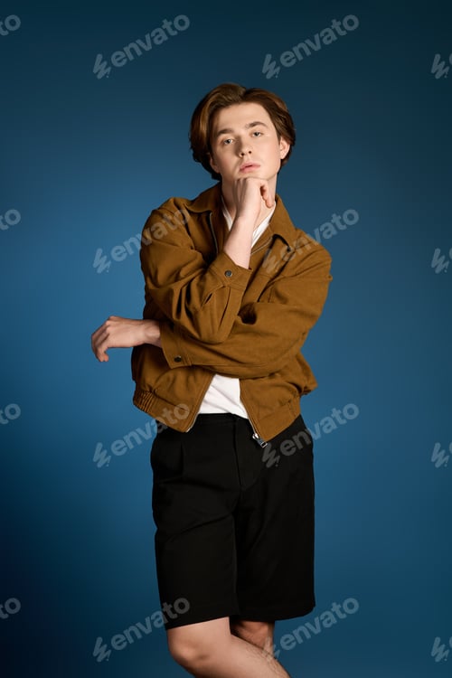 Preview: Fashionable young man poses thoughtfully against a vibrant blue background in stylish outfit