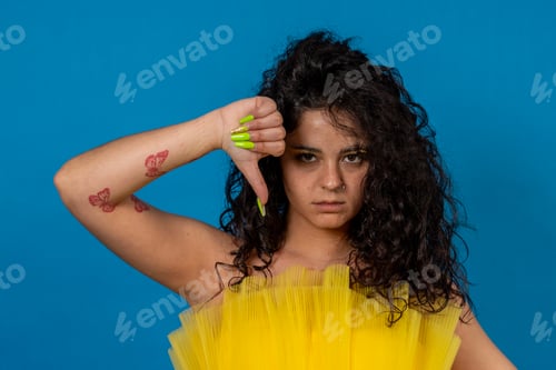 Preview: Young woman showing thumbs down gesture expressing disapproval on blue background