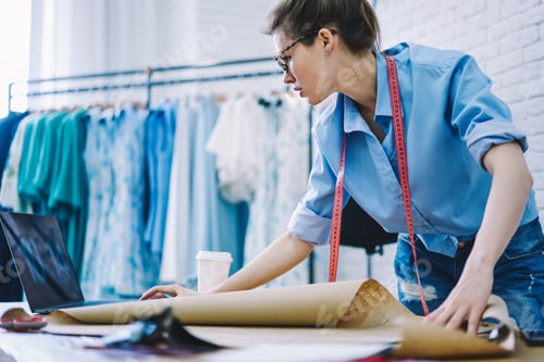 Preview: Focused dressmaker browsing laptop working in modern workshop