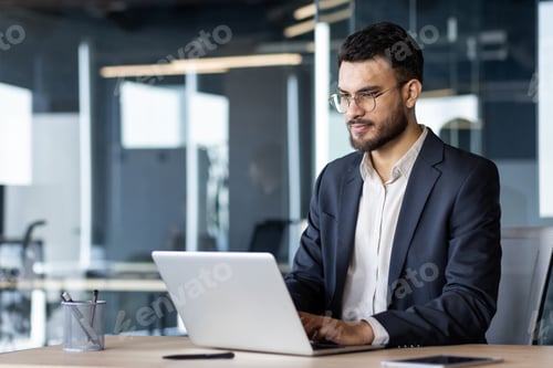 Preview: Focused businessman in modern office working on laptop, wearing glasses and suit, showcasing