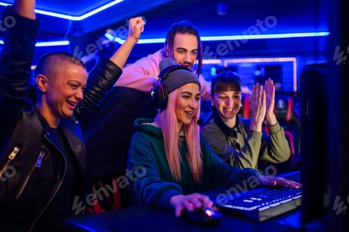 Preview: Gamer girl playing a video game in cybercafe while friends cheering.