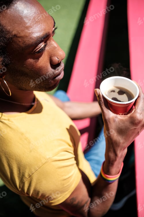 Preview: Portrait of non-binary person having a coffee sitting on colorful red bench.
