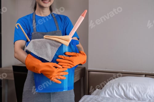 Preview: The cleaning lady wears orange rubber gloves and carries a bucket of bedroom cleaning supplies.