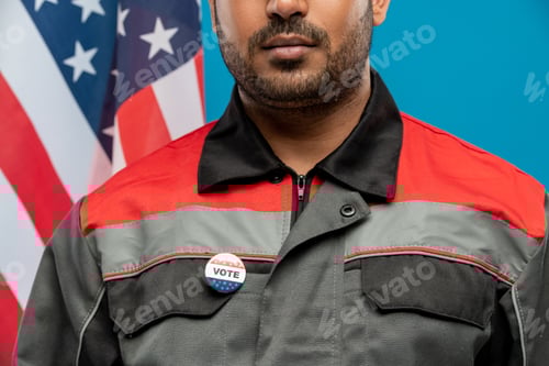 Preview: Young serious repairman of Hispanic ethnicity with vote insignia on uniform