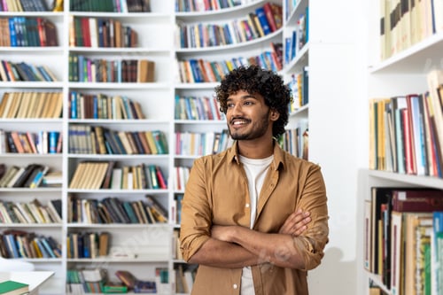Preview: Confident young man with curly hair standing in a library