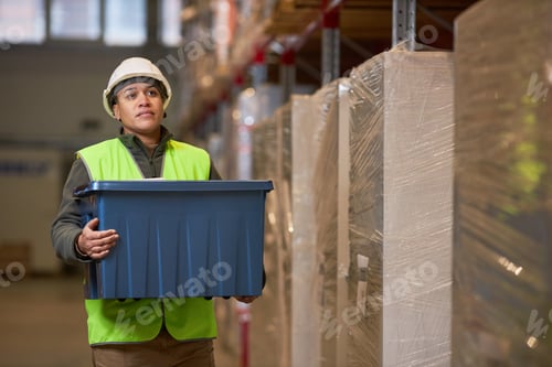Preview: Female worker carrying plastic box in indoor warehouse