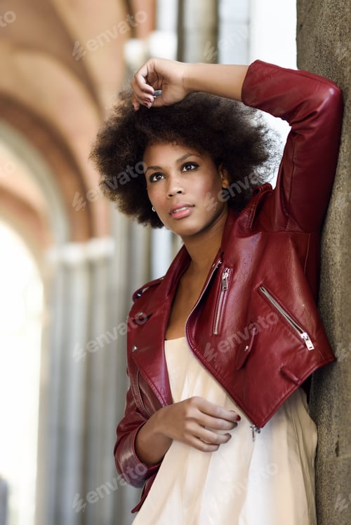 Preview: Young black female with afro hairstyle standing in an urban street. Mixed woman wearing red leather