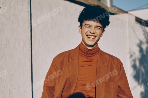 Preview: Portrait of a young man smiling, wearing a stylish rust colored jacket and turtleneck, set against a