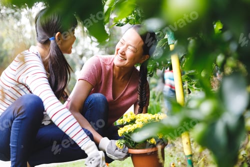 Preview: Happy asian mother and daughter smiling, wearing gloves and working in garden