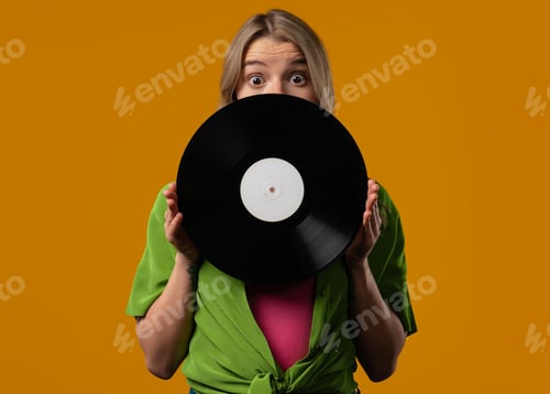 Preview: Pretty woman with vinyl record disc on yellow. Hobby, music lover, collection, nostalgia lifestyle.