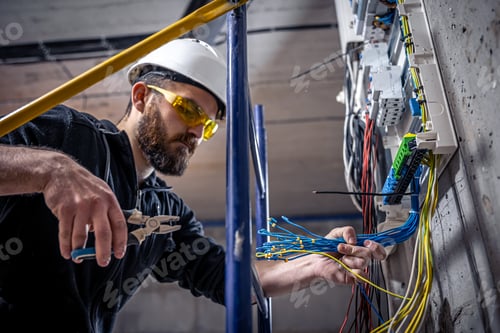Preview: A male electrician works in a switchboard with an electrical connecting cable.