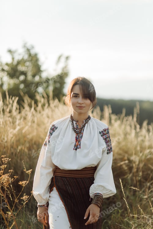 Preview: Young woman in traditional national embroidered shirt and skirt on nature at sunset.