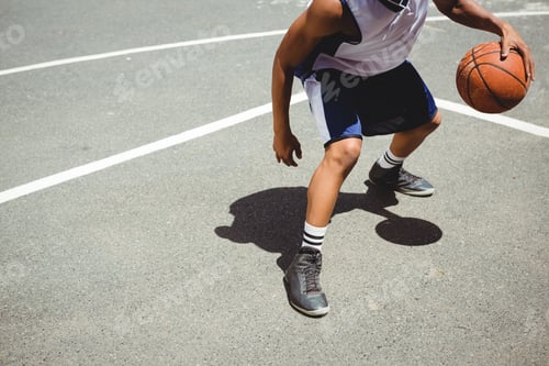 Preview: Low section teenage boy practicing basketball at court