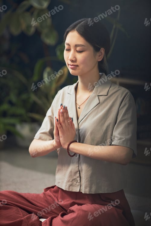 Preview: Young Adult Asian Woman Practicing Mindful Meditation with Hands in Prayer Pose